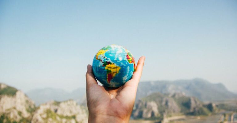 International Travel - Person Holding World Globe Facing Mountain